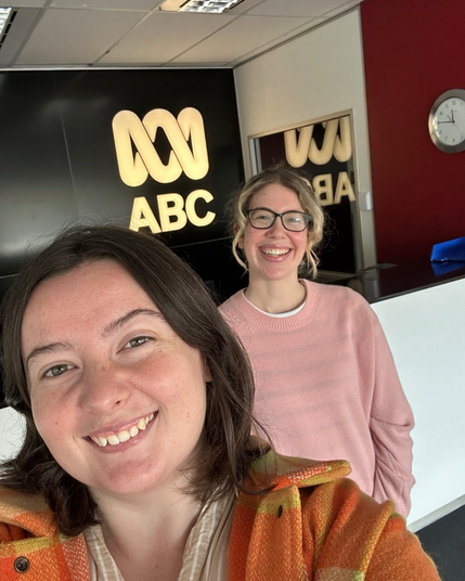 Two young women stand in front of a glowing ABC sign, smiling 