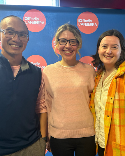 A man and two young women smile at the camera, behind them is an ABC radio Canberra banner 