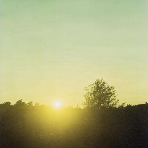 Sunset over a forest clad hill with outlines of some houses. Very light clouds, pastel blue sky.
