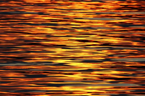 Photo of bright yellow and orange sunset light reflected on ripples in a lake.