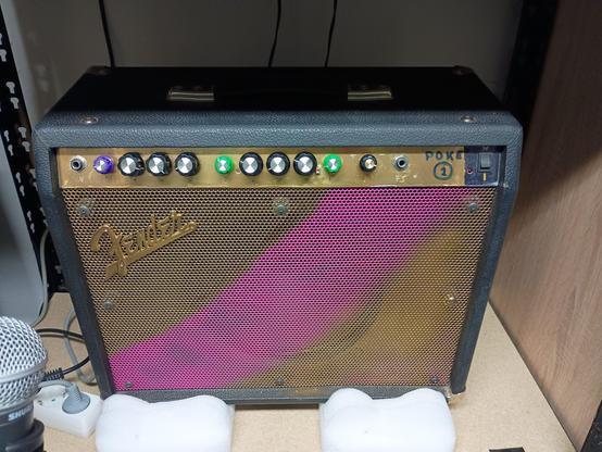 Ein Gitarrenverstärker in  Gold und Pink mit schwarzen, lila und grünen Drehreglern.