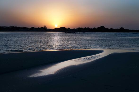 Sur le tiers supérieur de l’image, le soleil se couche derrière une langue de terre. Un bout de Méditerranée traverse l’image en son milieu, tel un fleuve calme. Sur la plage, qui occupe le tiers inférieur de l’image, un reflet humide découpe le sable sombre. 