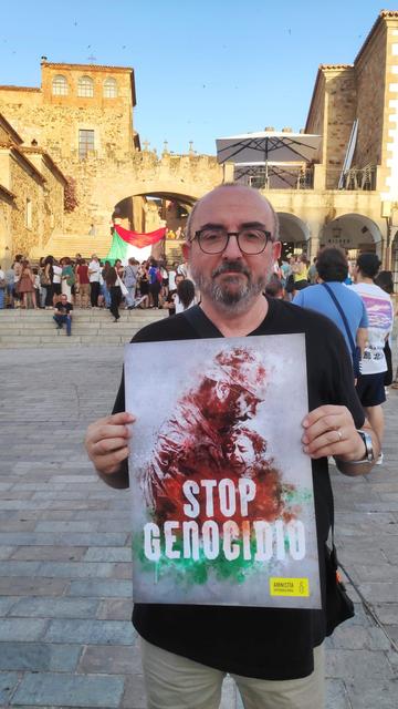 Un hombre, en la Plaza Mayor de Cáceres, sosteniendo un cartel con el lema STOP GENOCIDIO.