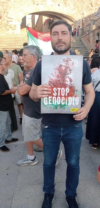 Un hombre, en la Plaza Mayor de Cáceres, sosteniendo un cartel con el lema STOP GENOCIDIO.