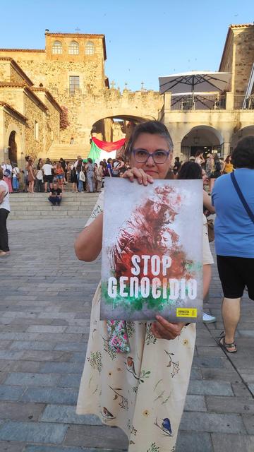 Una mujer, en la Plaza Mayor de Cáceres, sosteniendo un cartel con el lema STOP GENOCIDIO.