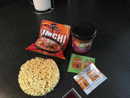 Afbeelding met Kimchi noedels en een potje kimchi en zakjes kruiden.