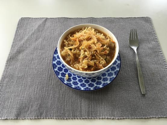 Afbeelding met het gerecht in een soepkom opgediend op een placemat en een fork er naast.