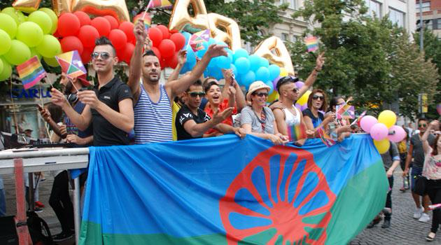 People at pride parade with colorful baloons holding roma flag
