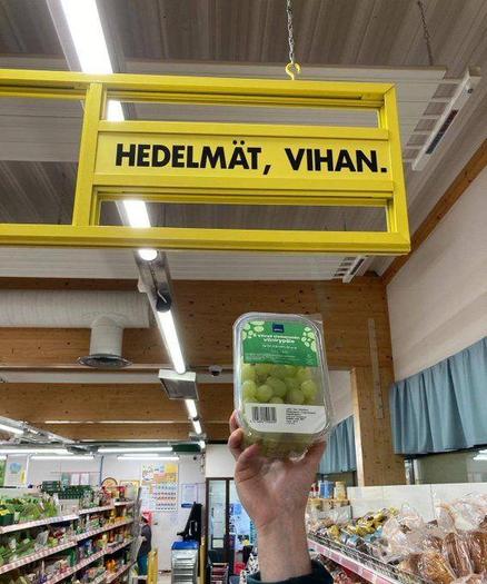 Kuva kaupan vihannesosastolta. Kädessä viinirypälerasia, yläpuolella kultti, jossa teksti "Hedelmät, vihan."