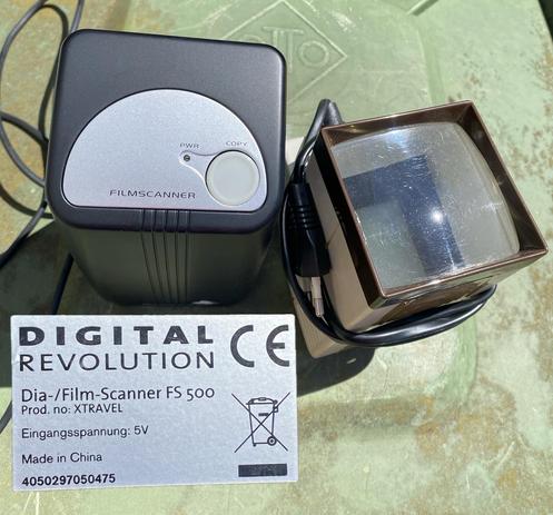 An image of a film scanner alongside its instruction label. The scanner is a compact, black device with a power and copy button on top. Next to it is a small, rectangular optical component with a transparent surface and a connected cable. The label indicates