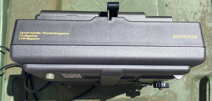 A close-up view of a device labeled with text in yellow, including "Gemeinschafts-/Standardmagazine," "CS-Magazine," "LKM-Magazine," and "AUTOFOCUS." The device has a textured surface and various