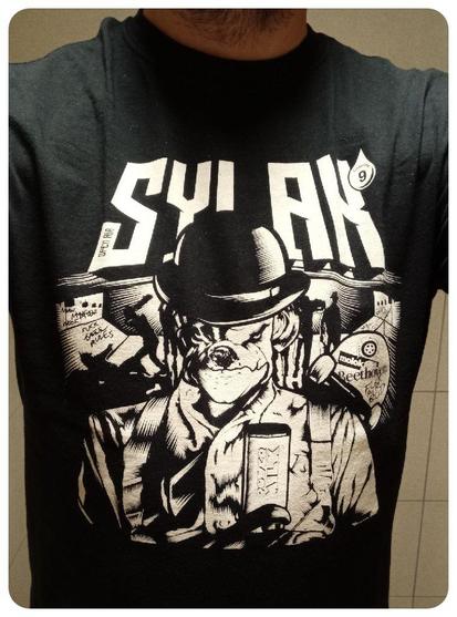 T-shirt noir du Sylak pour l'édition 2018. 
Chaque année on retrouve le chien, un bouledogue, mois en scène dans film de la culture pop. 
Cette année là, c'était Orange Mécanique. 
Donc le chien est grimé comme le petit Alex du film. 
Chapeau melon et faux sourcil. 
Dans des tons noir et blanc, ça reste soft et ça passe bien au boulot.