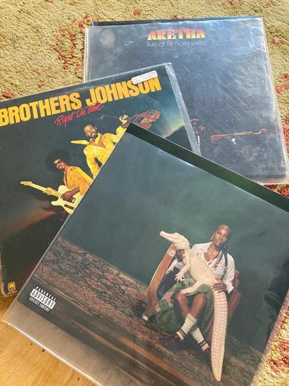 Three vinyl records: Alligator Bites Never Heal by Doechii, Right on Time by the Brothers Johnson, and Live at the Fillmore West by Aretha Franklin