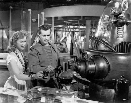 A man and a woman holding out cups for a robot who is pouring them coffee
