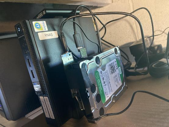 A computer with a bare hard drive next to it with wires coming out of it.