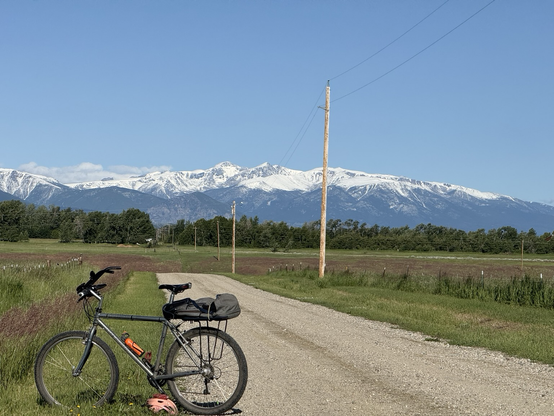 A rock hopper mountain bike on a gravel road. The high peaks of the Beartooths are covered by a late June snow under a blue sky.