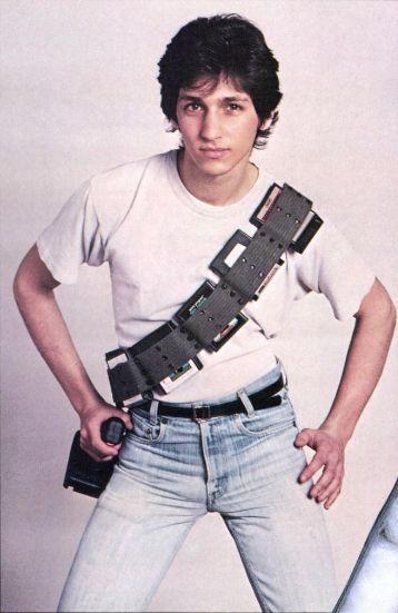 a kid with a 'cartridge belt' strapped across his white t-shirt, joystick in hand like a pistol, standing like a cowboy in a standoff. 80s humour.