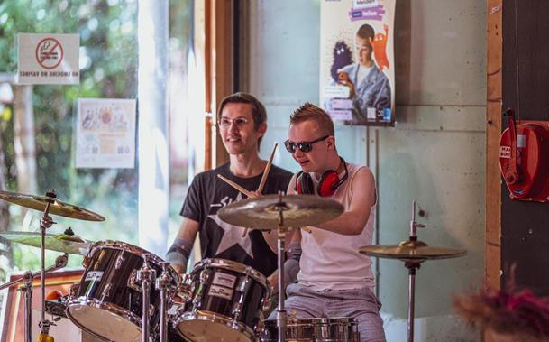 Two young men energetically playing drums together in a lively room filled with musical instruments.