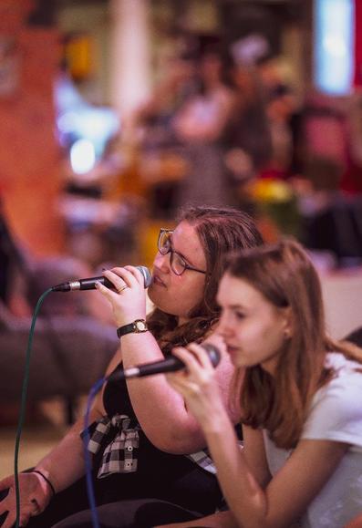 Two women singing into microphones, sharing a joyful moment in a cozy room filled with music and creativity.