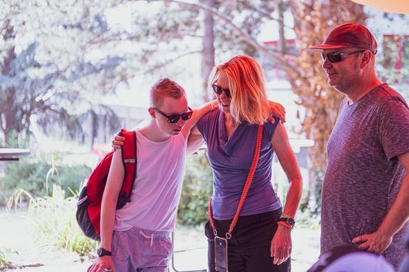 A young men, a women and a man pose next to a man with a backpack, all appearing cheerful in a natural environment.