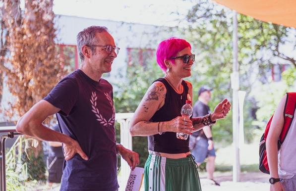Two people, the left one with vibrant pink hair, are smiling, creating a lively social atmosphere.