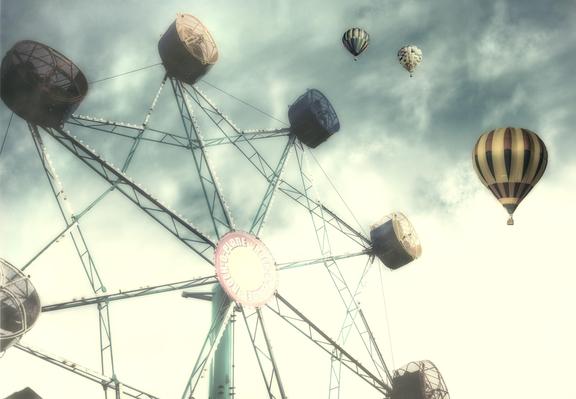 A Ferris wheel stands prominently against a bright, cloudy sky, accompanied by several hot air balloons floating nearby. The scene conveys a sense of nostalgia and whimsy, capturing an adventurous and leisurely atmosphere at the country fair.