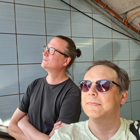 Selfie von Malte Schlorf und Michael Laven. Beide schauen nach oben. Hinter ihnen ist eine hellblau geflieste Wand.