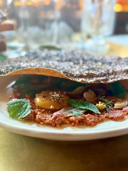 Leg of lamb kibbeh nayeh. Traditionally this is made with lamb and burgul and spices, but here it takes on a more traditional tartare style with mustard seeds and an egg yolk. The plate is covered with a crispy bread. 