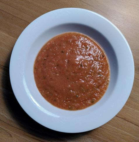 Weißer Teller mit oranger Gazpacho-Suppe.
