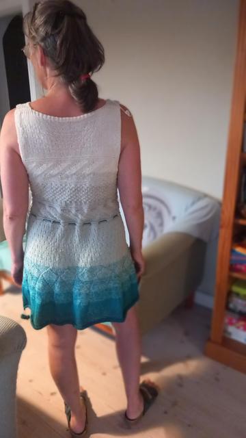 Femme portant une robe courte  tricotée en coton dans un dégradé turquoise à blanc,  vu de dos.