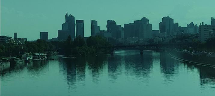 Vue depuis un pont sur la Seine, face aux tours de La Défense. Reflets calmes, lumière diffuse bleu-vert, ambiance orageuse douce
