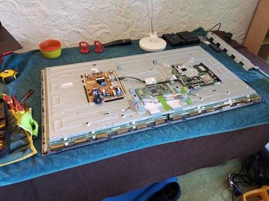 A flat screen TV lying face down on a table, the back has been removed. It's surrounded by tools.