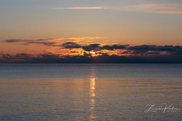 Sunrise over Lake Ontario, Toronto. Sun peeking through the clouds, sunlight reflected on the water.