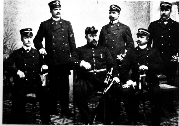 Länsmansfredag! Kirunas poliskår tidigt 1900-tal. Sittande i mitten syns Kirunas länsman, Carl August Olsson iförd tvåkantshatt. Han började som polischef i Luossavaara i januari 1900.   I slutet av 1800-talet var landshövdingen Husberg i Stockholm och såg då ett slagsmål. Plötsligt dyker en reslig konstapel upp och avbryter slagsmålet. Landshövdingen blev imponerad. En sådan man behövde han uppe bland rallarna i Lappland.   Han kontaktade senare Stockholm och det meddelades att den stora mannen var inspektionskonstapeln Carl August Olsson.