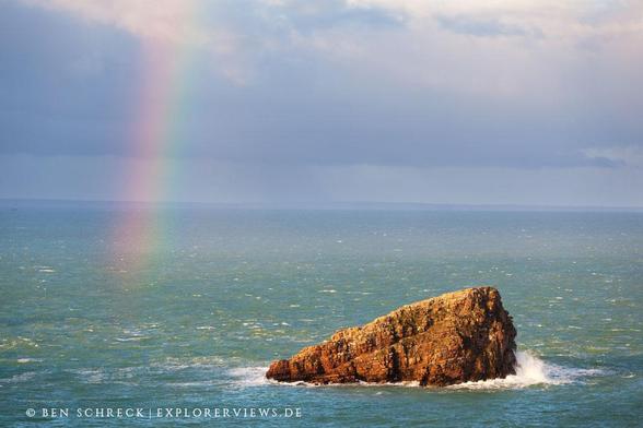 Blick übers Meer auf eine Felseninsel und einen Regenbogen