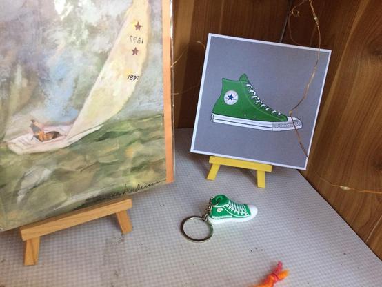 A print of an illustration featuring a green Chuck Taylor shoe, and a key chain that (almost) matches it. (Also a sailboat image.)
