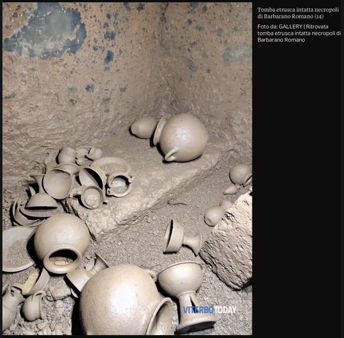 Inside an Etruscan tomb chamber, numerous intact and broken clay jugs and bowls lie on a stone platform and the dusty ground.