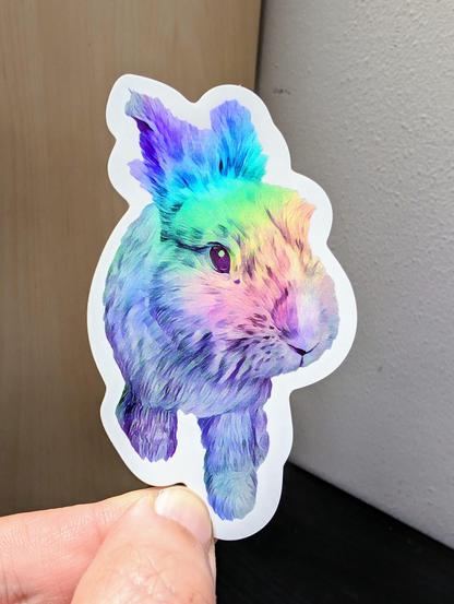 Photo of a left hand holding a diecut sticker. The sticker is a holographic rabbit drawing.