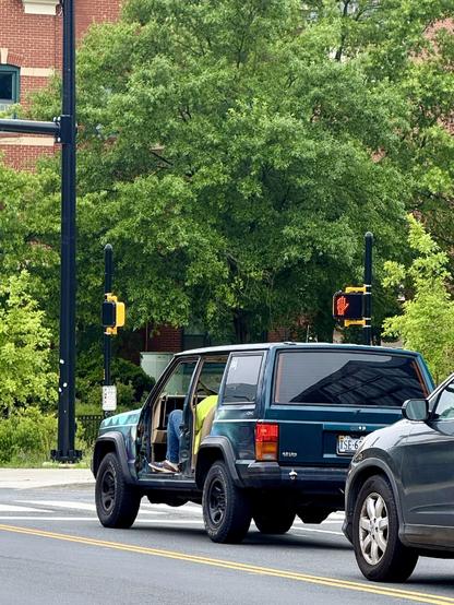 An older model Jeep SUV missing two doors on the drivers side (it’s also missing the other doors, but that can’t be seen from this angle). 