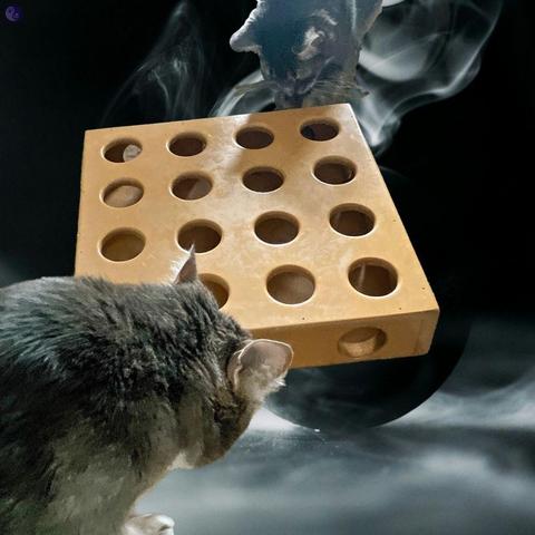Two gray tabby cats examine a light wooden puzzle box with round holes all over it, floating above a black ball giving off gray smoke, affecting the top gray cat, in the smoke, who is glowing.