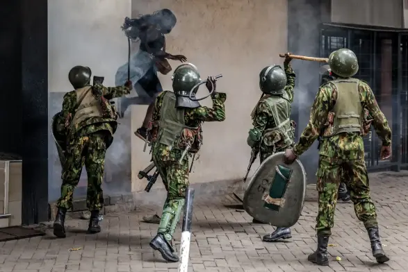 A protester jumps for safety as she emerges from a narrow alley while Kenyan police officers strike her with whips and clubs.