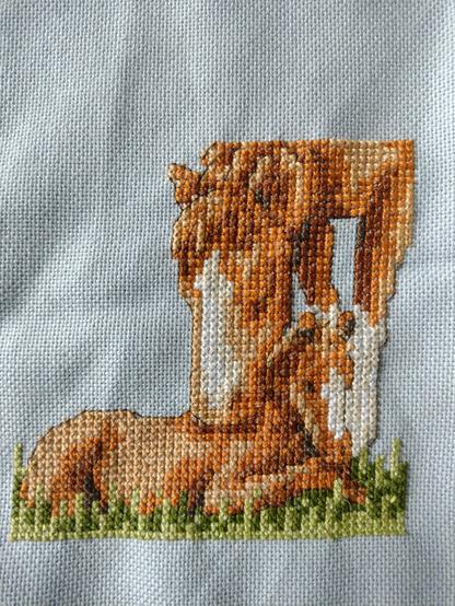 Kruissteek borduurwerk van een liggend veulen met de moeder, beide voskleurig.