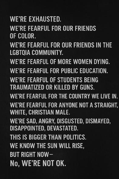 A black background displays bold white text expressing collective emotional exhaustion and fear. Each line begins with “WE’RE,” addressing issues like racial injustice, threats to LGBTQIA people, violence against women, public education, gun violence, and rising hate. The message culminates with: “THIS IS BIGGER THAN POLITICS. WE KNOW THE SUN WILL RISE, BUT RIGHT NOW – No, WE’RE NOT OK.” The tone is somber and urgent.