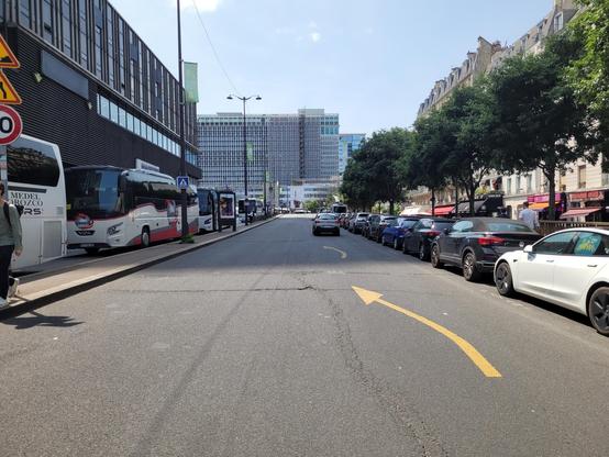 Massively overwide street leading to Montparnasse station, with a column of cars parked on one side, buses on the other.