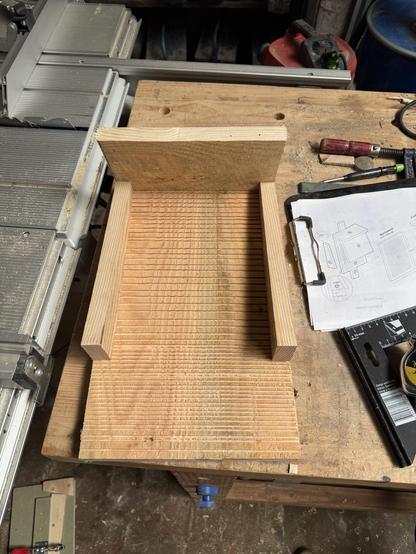 A wooden workpiece in a workshop setting, featuring a groove design. Nearby tools and a project blueprint are visible, along with a workbench surface.