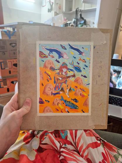 Voici la photo d’un dessin que j’ai tout juste terminé, aux crayons de couleur. On y voit un personnage assis sur une pierre, jouant du luth, entouré de poissons colorés qui sortent de la bouche de grandes têtes de pierre qui chantent. Le dessin est encore scotché à son support de travail, maintenu par du scotch papier, et je le tiens sur mes genoux, posés sur une robe fleurie. L’ensemble est dans une palette vive de bleus, oranges, rouges et jaunes.
j’ai gardé toutes mes petites annotations sur les côtés, comme d’habitude.