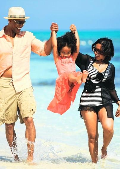 At the beach a mother and father swing Thier little daughter up in the air for fun