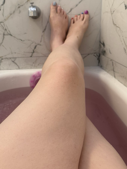 Thick thighs going off into the distance in a warm, purple bath, with beautifully painted Pride flag toes at the end of each foot