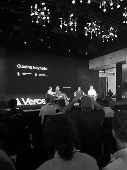 The closing fireside chat with Guillermo Rauch (Vercel CEO) and Brendan Eich (JavaScript creator) discussing the future of the web.

Four people in total are sitting on a stage. Part of the audience is visible below. Above and behind you see the projection screen display the names of the two main speakers along with the text "Closing keynote"