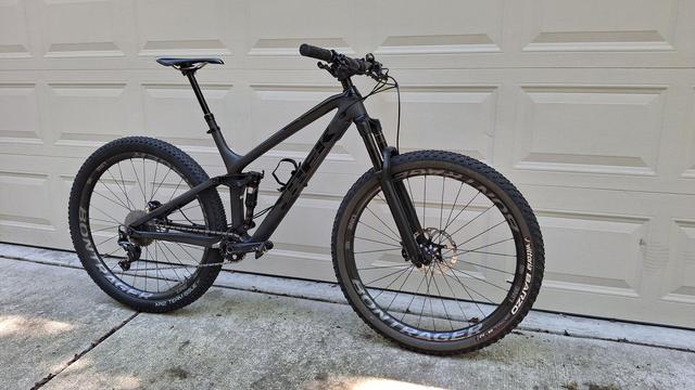 Black full suspension mtb leaning against a tan garage door.